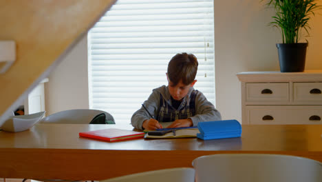 front view of caucasian boy doing his homework at dining table in a comfortable home 4k