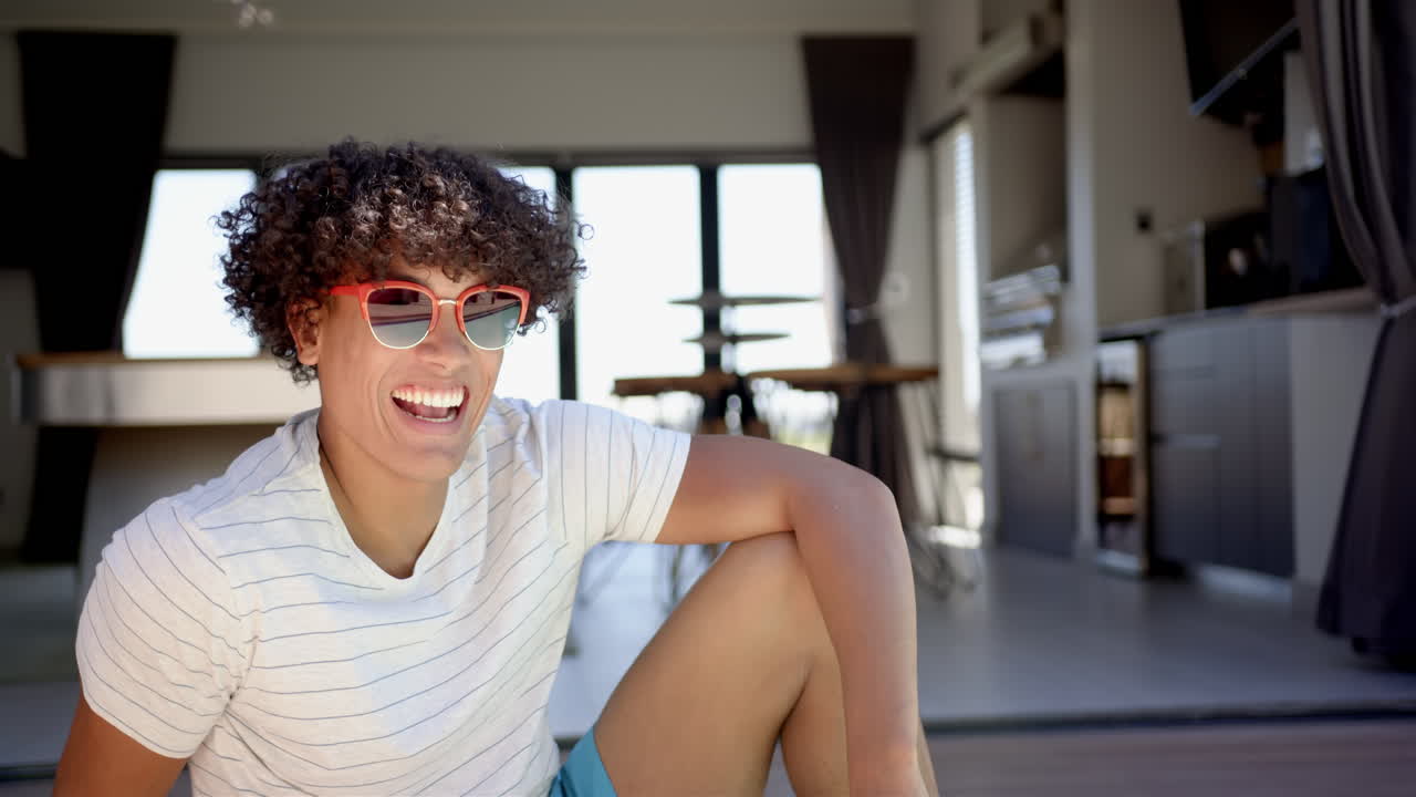 Smiling man wearing sunglasses sitting on floor in modern home interior, copy space