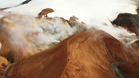 people walking on the ridge of steaming mountain in kerlingarfjoll geothermal area in highlands of iceland - aerial drone