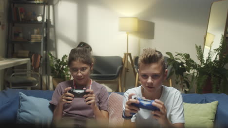 two children playing video games on a sofa at home