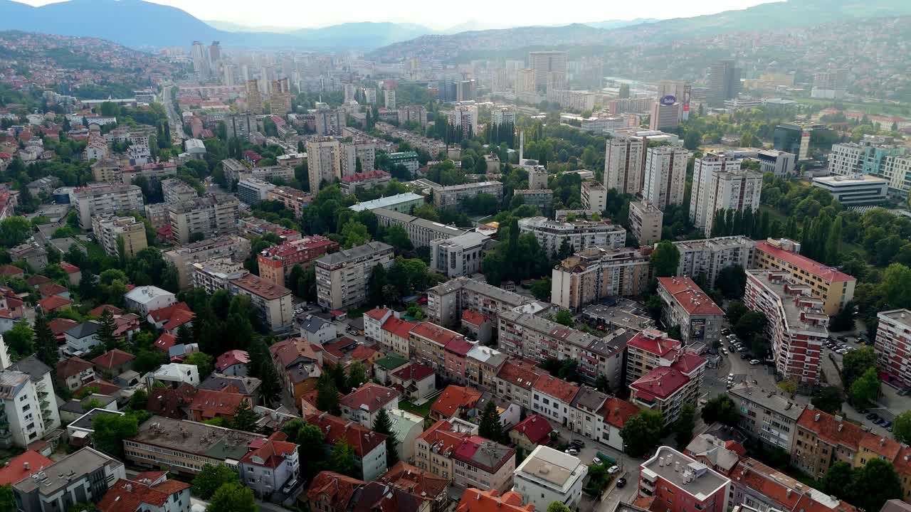 Aerial drone view of Sarajevo, capital of Bosnia and Herzegovina, showing a mix of Ottoman, Austro-Hungarian, and modern architecture nestled among surrounding mountains at sunset
