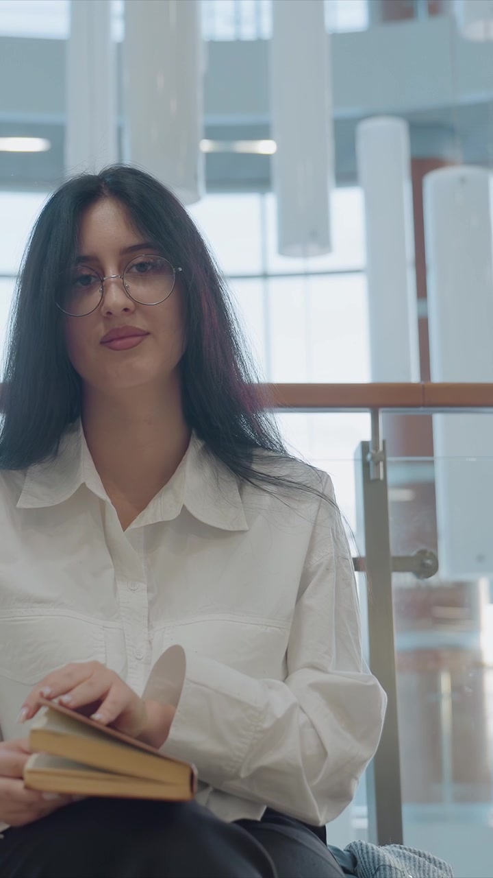 Primer plano de una mujer leyendo un libro. La escena muestra a la mujer sosteniendo y pasando páginas con detalles finos. La luz natural llena el fondo, sugiriendo grandes ventanas, y mostrando a la mujer con su libro.