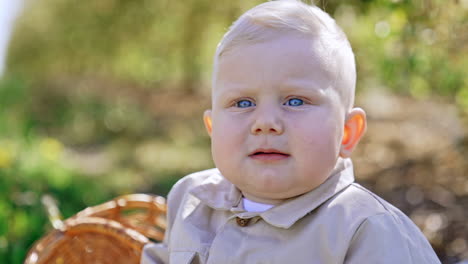adorable baby with cute plump cheeks and blue eyes. portrait of a lovely kid sitting outdoors. close up. blurred backdrop.