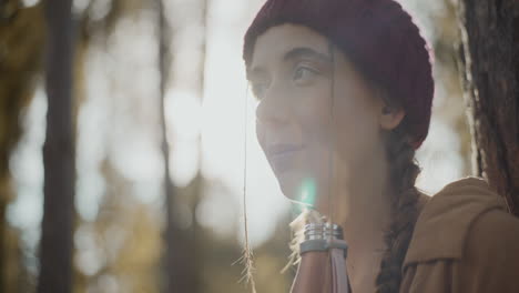 Woman-wearing-knitted-hat-with-open-bottle-in-forest