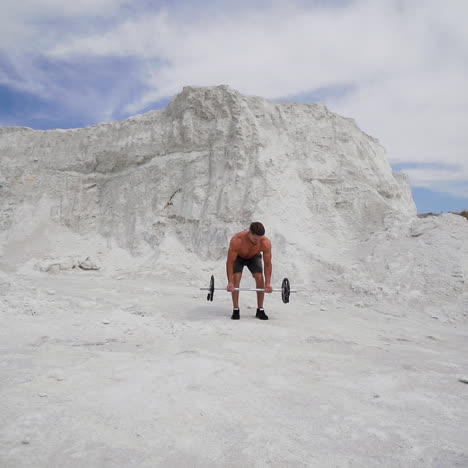 strong shirtless athlete taking heavy barbell outdoors. muscular man lifting barbell on white mountain background. slow motion.