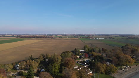 Slow-aerial-dolly-above-coastal-home-settlement-with-farmlands-and-wind-turbines-behind