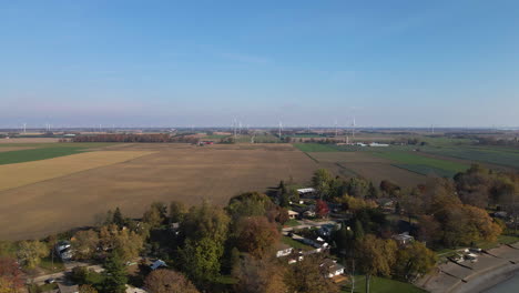 slow aerial dolly above coastal home settlement with farmlands and wind turbines behind