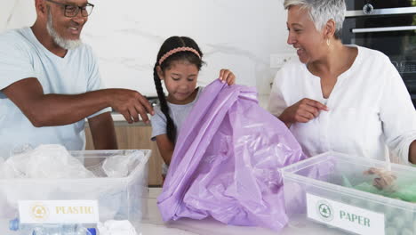 biracial family sorts recycling, with a granddaughter placing plastic in a bin