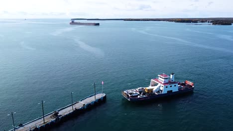 barco de ferry que sale del muelle con un buque de carga detrás