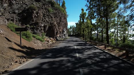 hombre caminando en una carretera de montaña, ladera alta de la montaña, árboles verdes, cielo azul