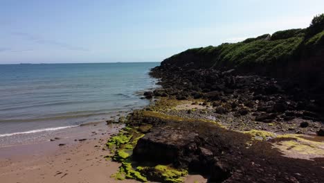 Aerial-view-Traeth-Lligwy-Jurassic-rocky-weathered-rugged-Anglesey-coastal-seascape,-push-in-low