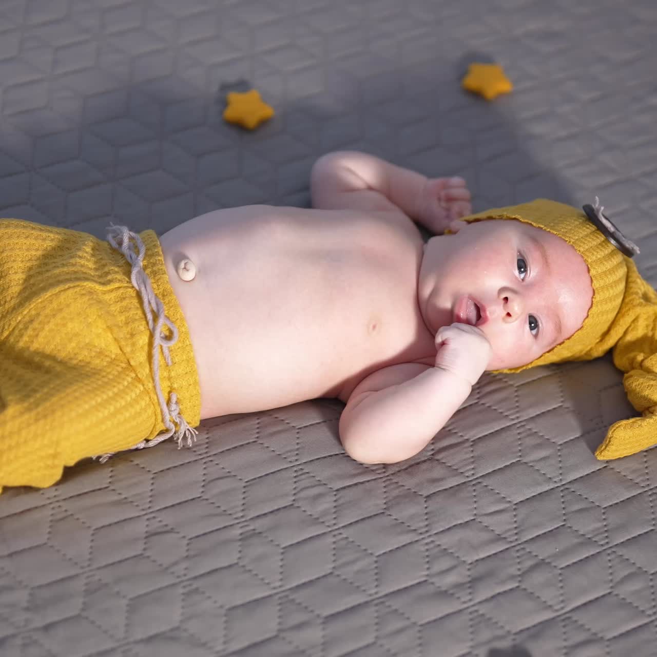 Baby wearing funny long cap and pants on the bed. Toy stars around a boy in a funny costume. Kid with naked belly on the bed. View from above