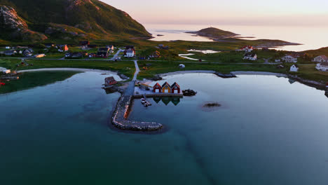 Drone-approaching-colorful-rorbuer-at-a-pier,-midnight-sun-in-North-Norway