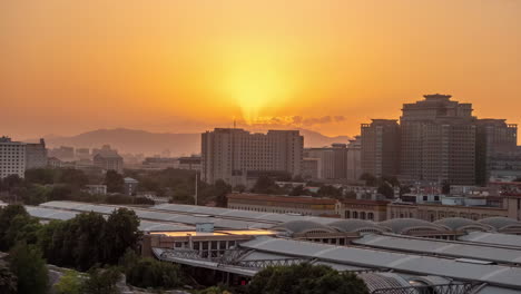 Cinematic-metropolitan-rising-shot-over-tower-in-downtown-urban-city,-Train-station-together-with-landmark-building-skyscrapers-towards-the-city-skyline-at-orange-sunset