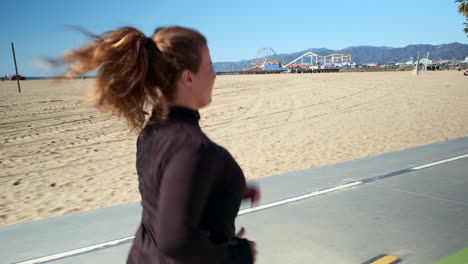 mujer en forma enfocada trotando en el camino de la playa santa monica california en una dura mañana soleada