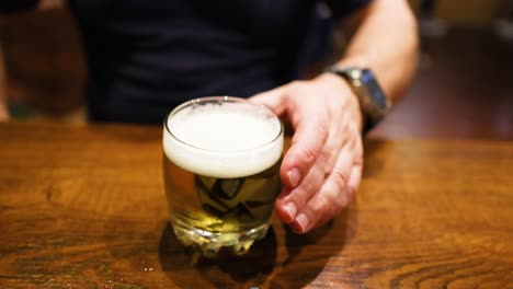 man reaches for beer glass on table