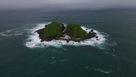 pequeña isla rocosa con olas espumosas en la reserva natural de la isla solitaria dividida cerca de la costa de la playa de zafiro en nsw, australia