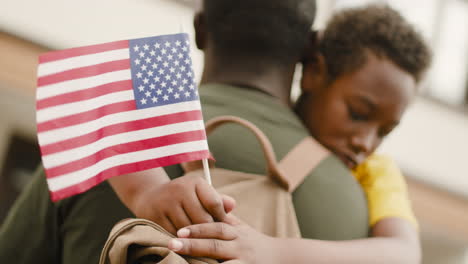 porträt eines traurigen jungen, der eine usa-flagge hält und seinen nicht erkennbaren militärvater umarmt 1