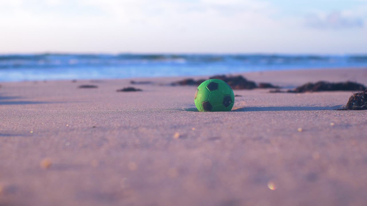 bola verde en la arena, basura y desechos en una playa vacía de arena blanca del mar báltico, problema de contaminación ambiental, luz de la hora dorada en la noche, tiro medio