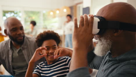 grandfather wearing vr headset as multi-generation male family sit on sofa at home together