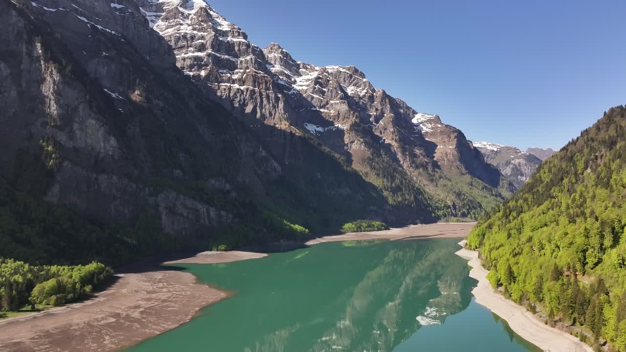 Aerial view of Klöntalersee lake reflecting snowy alpine peaks and lush green forests in Glarus, Switzerland