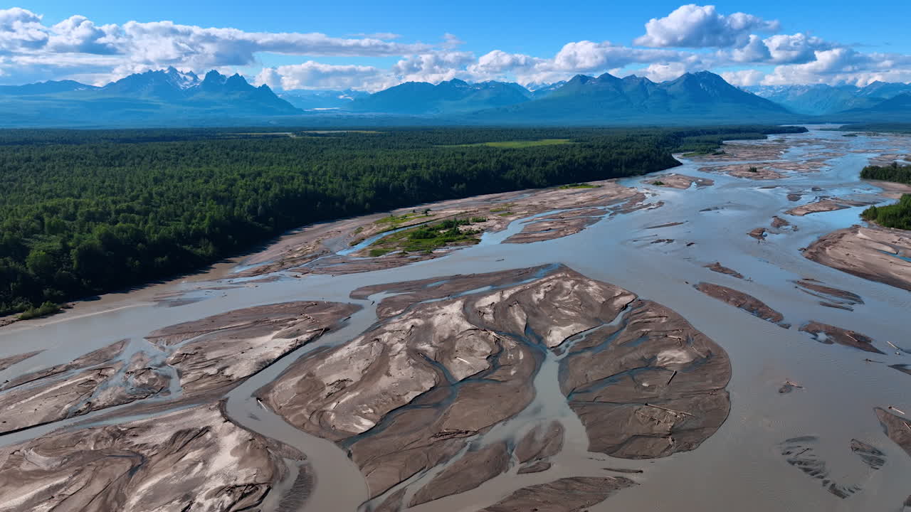 Splendido delta di fiume poco profondo con ramificazioni, circondato da rigogliosi boschi verdi. Catena montuosa e nuvole soffici sullo sfondo. Alaska. Vista aerea