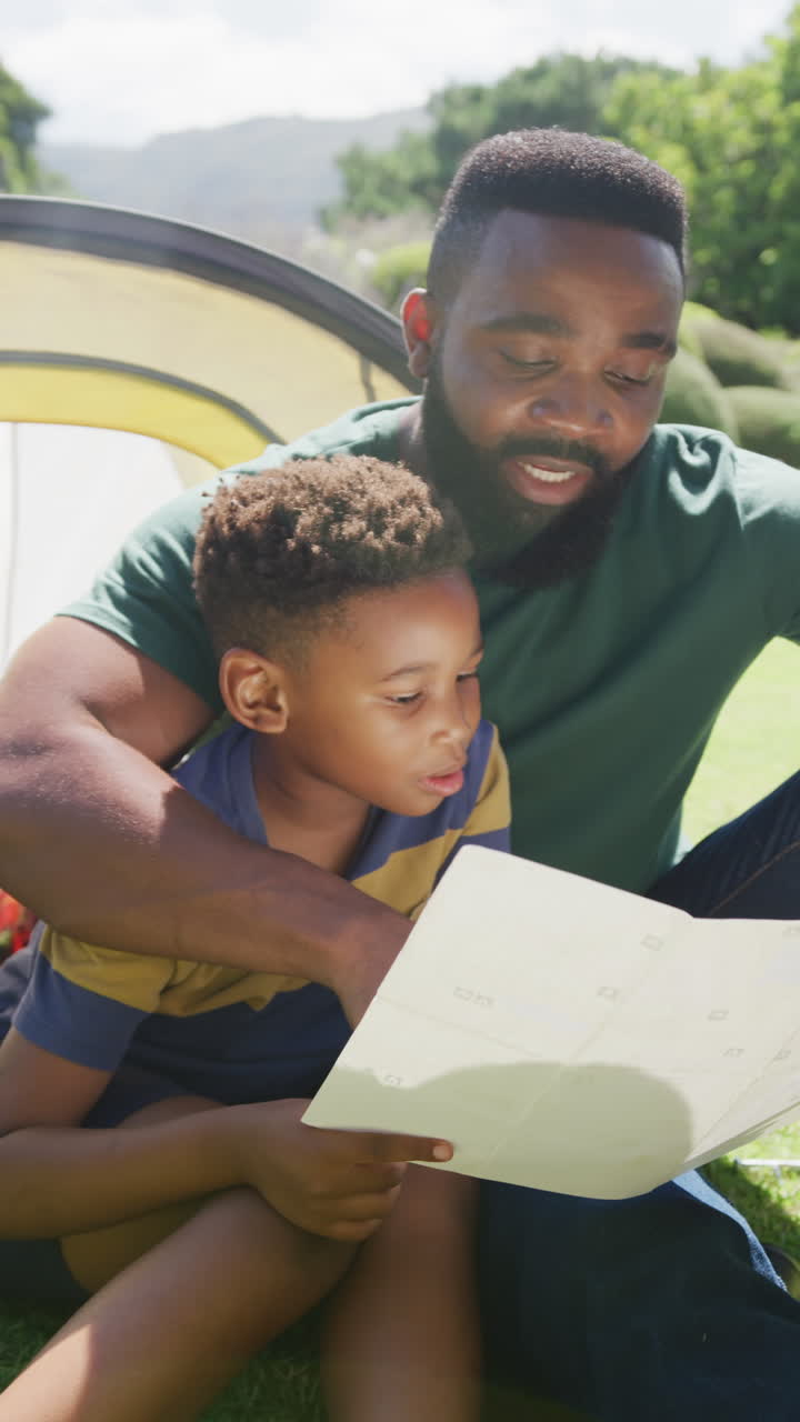 Video verticale di padre e figlio afroamericani seduti in tenda a leggere, al rallentatore