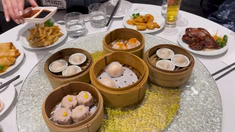 a table spread with dim sum, bamboo baskets, and sauces. hands reach for food, creating a lively dining atmosphere