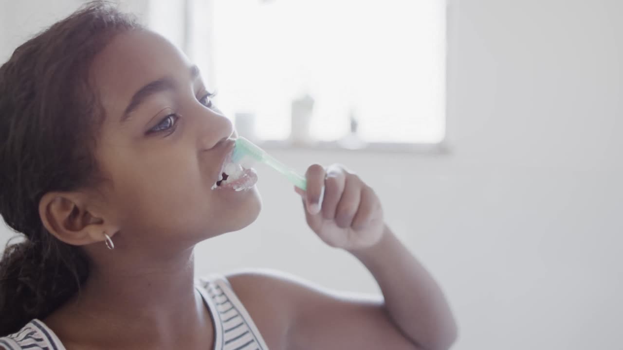 Happy african american girl brushing teeth in bathroom, slow motion