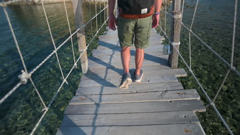 Male-walking-across-a-wooden-bridge-out-to-a-island-surrounded-by-beautiful-clear-blue-ocean-water