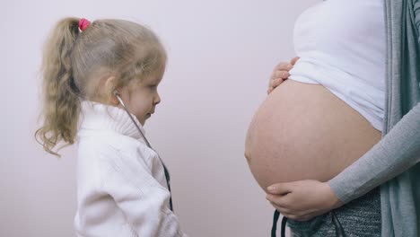 funny-girl-touches-pregnant-mother-tummy-with-stethoscope