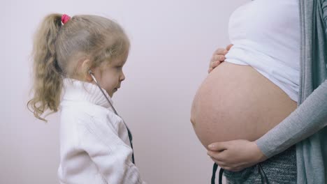 chica divertida toca el estómago de la madre embarazada con un estetoscopio