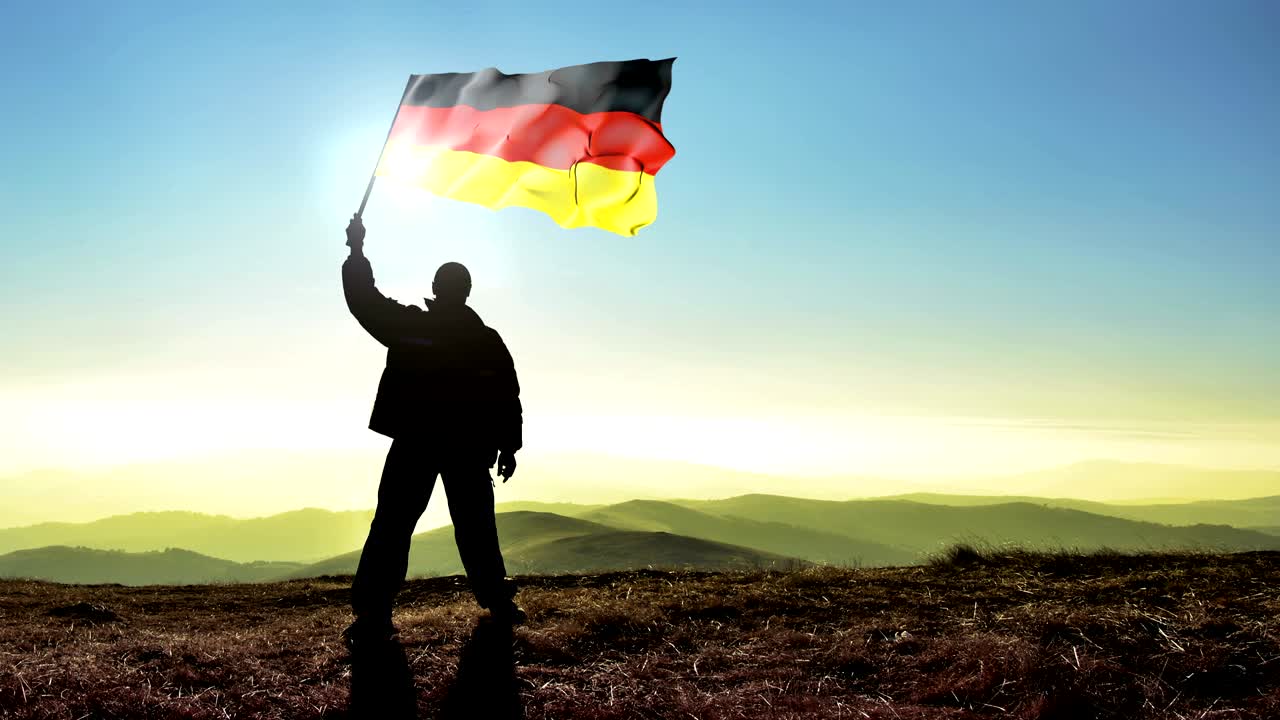 Silhouette di uomo vincitore di successo che sventola la bandiera tedesca sulla cima della montagna. Sfondo Cinemagraph in LOOP