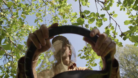 man on riding mower with mosquito head net, upward pov from under steering wheel