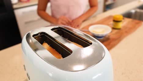 a person prepares toast in a bright kitchen, focusing on a toaster and bread. warm lighting enhances the cozy atmosphere