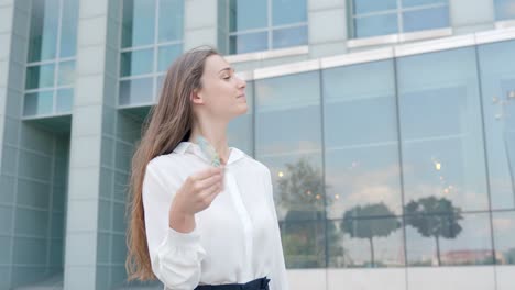 corporate woman happily waving euros in front of office building