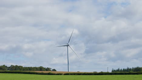 a single wind turbine spins steadily in a green rural landscape near edinburgh, scotland. daylight, soft natural lighting, and a static wide shot capture the serene environment