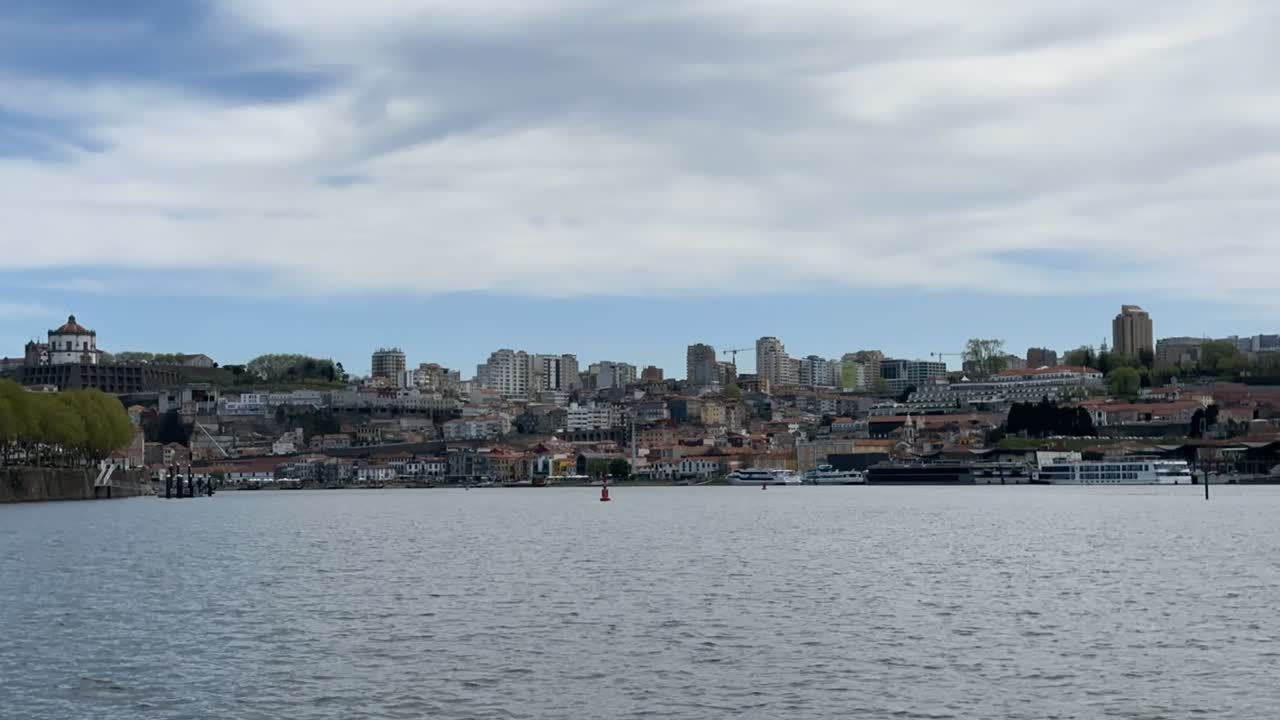 Daytime view across Douro River in Porto showing Dom Luís I Bridge and hilltop Serra do Pilar Monastery. City buildings rise along hillside with seagulls flying over calm water under blue sky