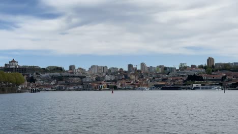 daytime view across douro river in porto showing dom luís i bridge and hilltop serra do pilar monastery. city buildings rise along hillside with seagulls flying over calm water under blue sky