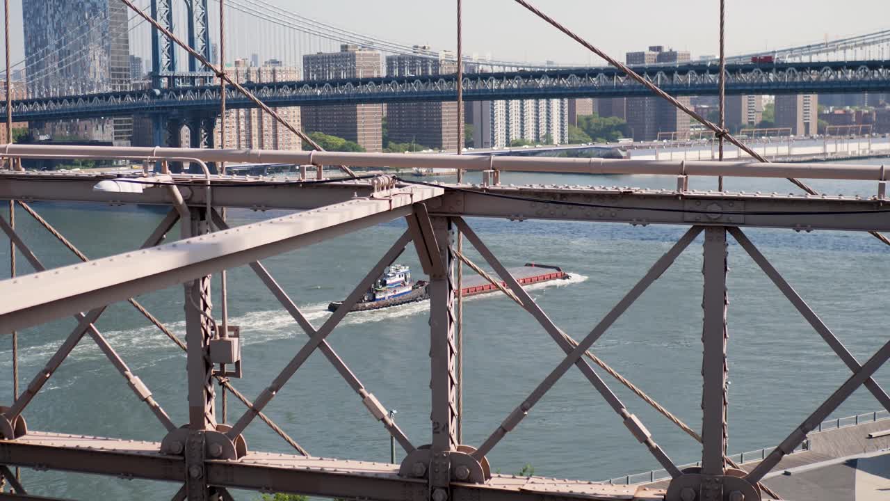 Slow motion landscape of barge cargo shipping freight boat with Manhattan Brooklyn bridges structure East River New York city skyline CBD USA America travel transport tourism industry