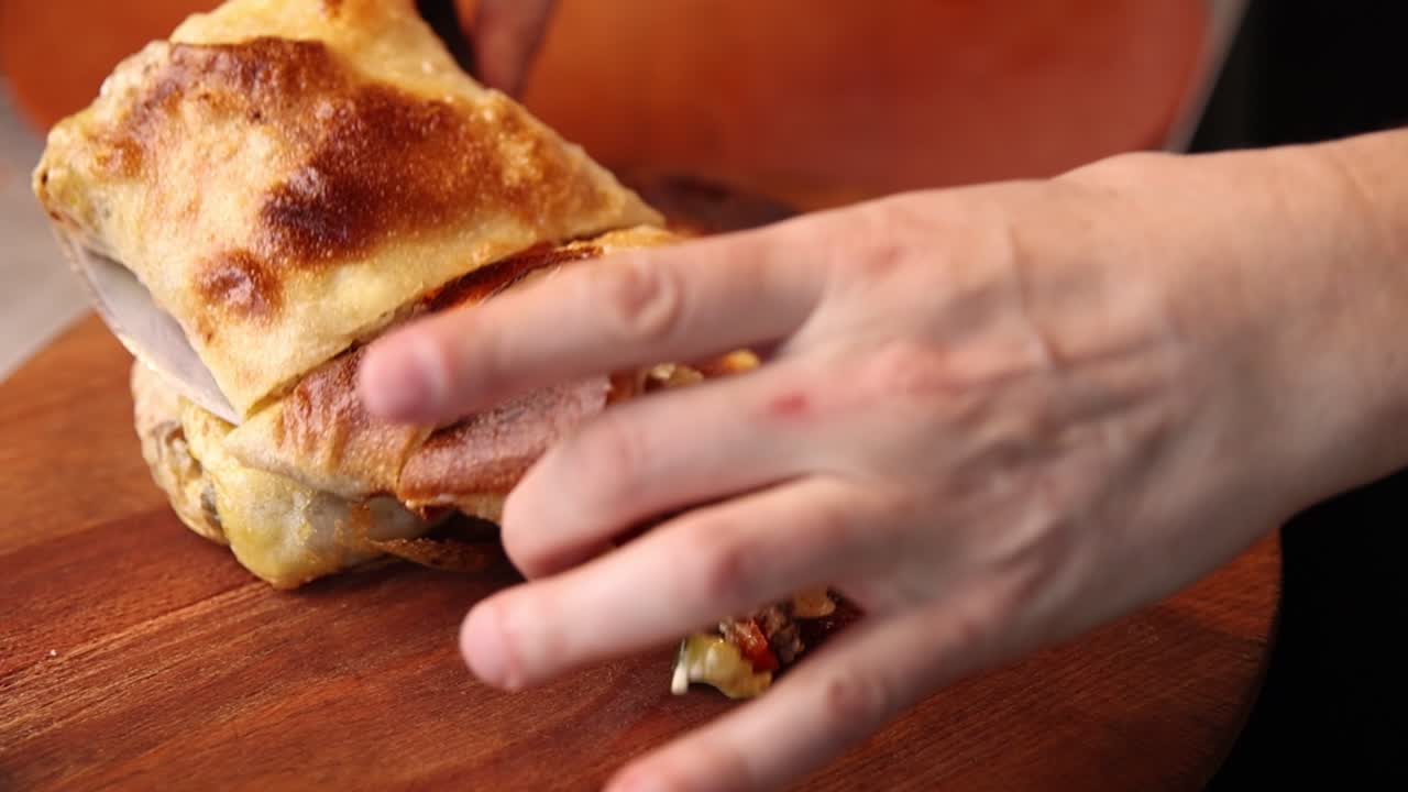 Primo piano di mani che tagliano un pasticcino salato dorato e appena sfornato