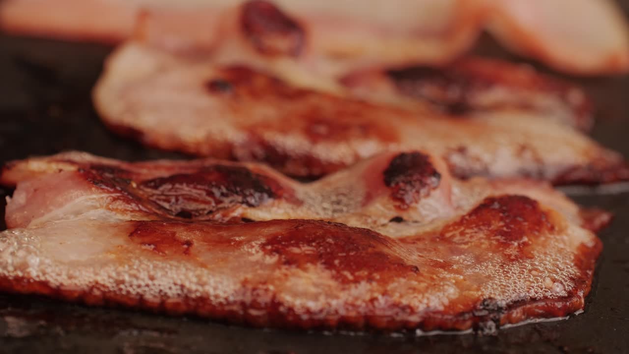 Cooking bacon slice for burgers on the grill close-up macro. The chef in kitchen of the restaurant making cutlets for smash burgers - smash burger beefsteak. Fast and street food concept. High quality 4k footage
