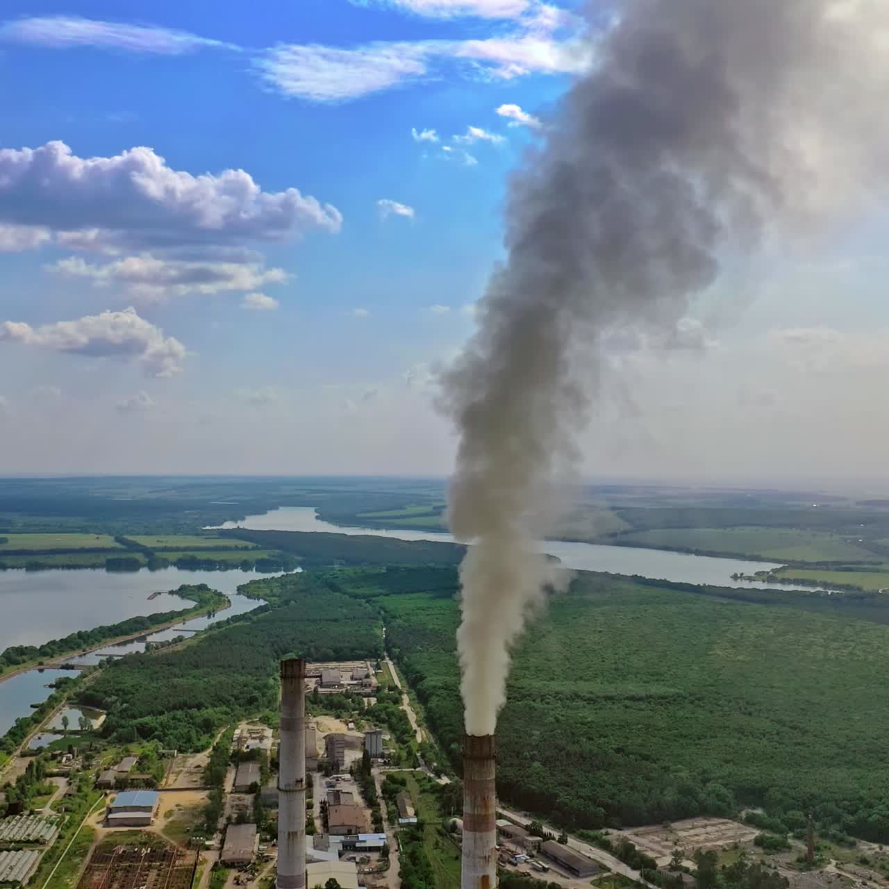 Dirty smoke from industrial pipe. Manufacturing with pipes on nature background with green fields and river. Pollution of environment.