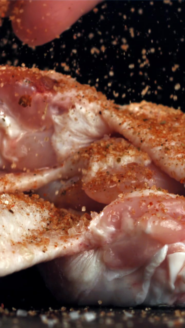 Primo piano al rallentatore di pollo crudo che viene condito con spezie