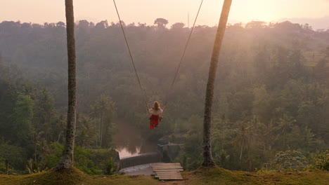 slow motion woman swinging over tropical rainforest at sunrise travel girl sitting on swing with scenic view enjoying freedom on vacation having fun holiday lifestyle