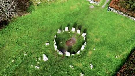 Top-down-aerial-drone-shot-rising-up-over-the-Drombeg-Stone-Circle,-an-ancient-historical-landmark-in-County-Cork,-Ireland