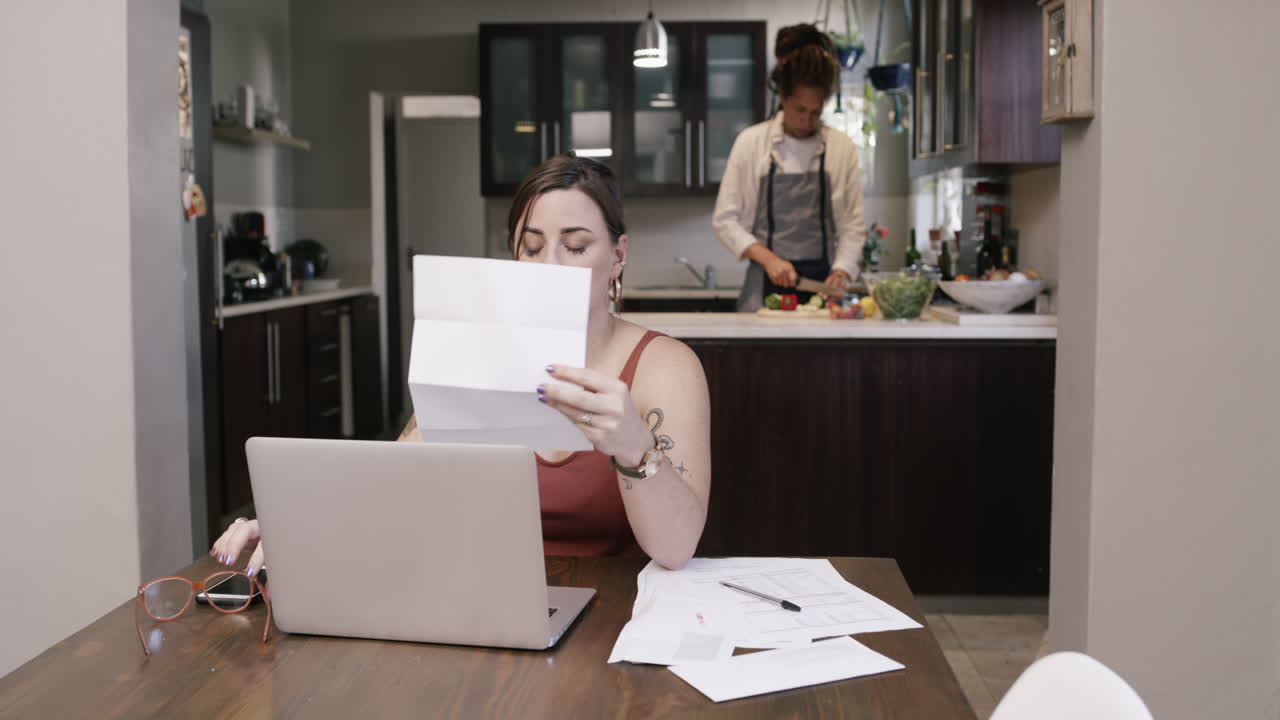 Coppia al lavoro in cucina; donna che guarda documenti e stressata