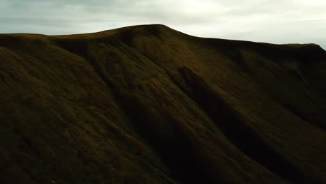 aerial landscape view of icelandic highlands dark mountains, covered in bright green grass, on a cloudy day