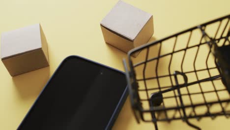 video de un teléfono inteligente con pantalla en blanco, cajas, carrito de compras sobre fondo amarillo