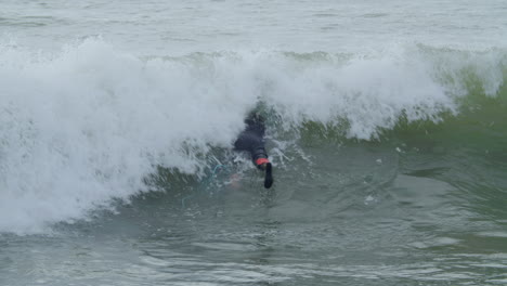 sportive man in wetsuit with artificial leg lying on surfboard and swimming in the ocean when a wave covering him 1